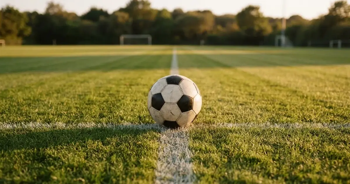 Ein Fussball liegt auf dem Mittelkreis eines Rasenfelds, die weissen Linien kreuzen sich auf dem gepflegten Gras im warmen Abendlicht.