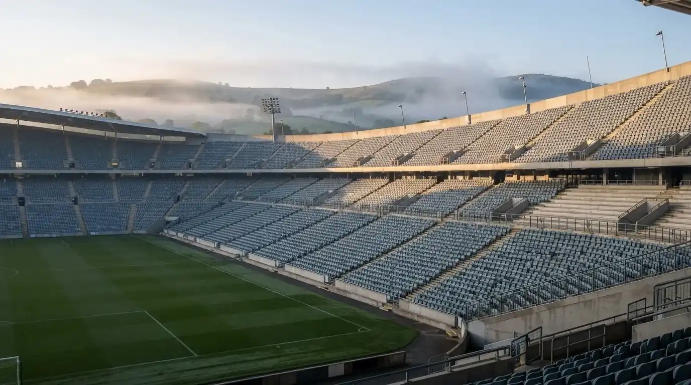 Ein leeres Stadion im Morgenlicht mit Blick auf die Sitzreihen, im Hintergrund Hügel und aufsteigender Nebel.