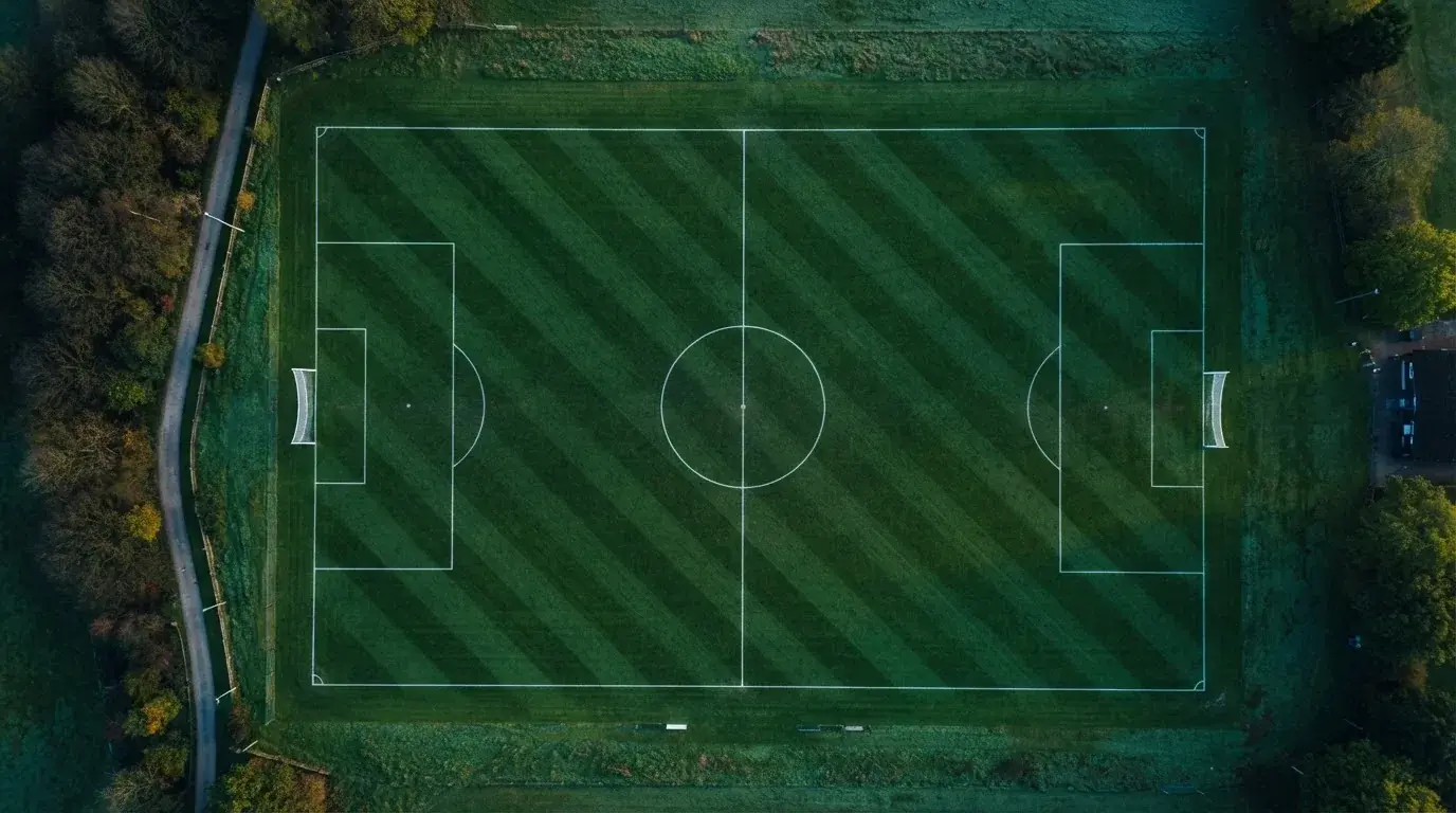 Ein Fussballplatz von oben gesehen, die Linien bilden ein helles Muster auf dem Rasen, Drohnenperspektive in der Morgendämmerung.